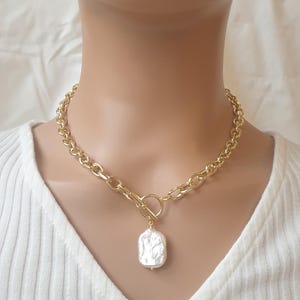 May include: A gold chain necklace with a large, white baroque pearl pendant. The chain is a thick, chunky style.