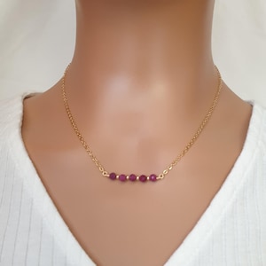 May include: A gold chain necklace with a row of small, dark purple beads.