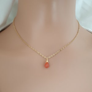 May include: A delicate gold chain necklace with a single teardrop-shaped orange gemstone pendant.