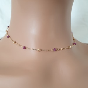 May include: A gold chain necklace with small, round, dark red gemstones. The necklace is on a mannequin's neck.