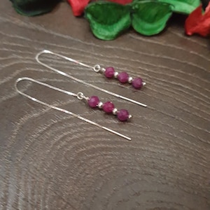 May include: A pair of silver chain earrings with multiple small, dark pink gemstone beads.