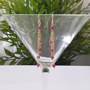 Peut inclure: Boucles d'oreilles en chaîne dorée avec des perles de pierres précieuses rouges pendantes.