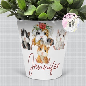 Könnte beinhalten: Weißer Keramiktopf mit einem Meerschweinchen, das ein Blumenband trägt, drei weiteren Meerschweinchen und dem Namen "Jennifer" in brauner Kursivschrift.