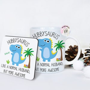 May include: A white mug and a coaster with a blue dinosaur illustration. The mug and coaster both say "Hubbysaurus" and "Like a normal husband, but more awesome".