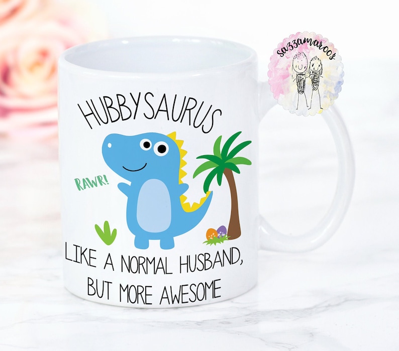 May include: White ceramic mug with a blue dinosaur illustration and the text "Hubbysaurus, Rawr! Like a normal husband, but more awesome".