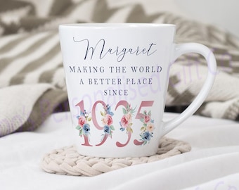 May include: White ceramic mug with a floral design and the text "Margaret Making the World a Better Place Since 1935".
