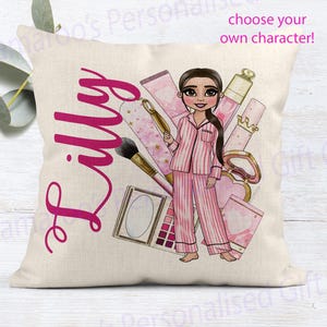 May include: A square cushion in beige, featuring a pink illustration of a person in striped pyjamas with makeup items. The name "Lilly" is written in pink cursive. Text reads "choose your own character!"