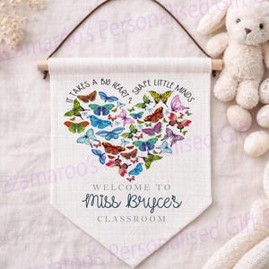 Peut inclure: Une bannière de classe personnalisée avec un cœur composé de papillons colorés. La bannière porte l'inscription "It takes a big heart to shape little minds" et "Welcome to Miss Bryce's Classroom."