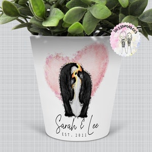 May include: White ceramic planter with a pink watercolour heart and two penguins inside. The planter has the text "Sarah & Lee EST. 2011" printed on the bottom.