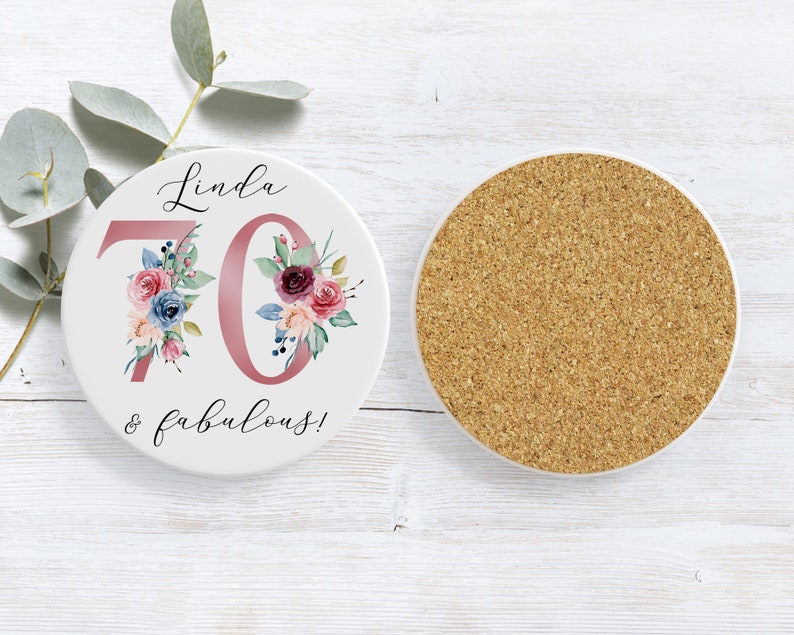 Puede incluir: Posavasos de cer&aacute;mica blanca con un dise&ntilde;o floral rosa y el texto "Linda 70 & fabulosa!"