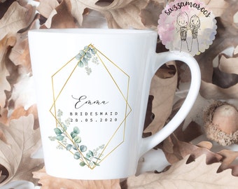 May include: White ceramic mug with a gold geometric frame and green eucalyptus leaves. The mug has the text "Emma Bridesmaid 28.05.2020" printed on it.