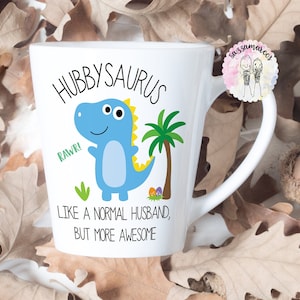 Peut inclure: Une tasse en céramique blanche avec une illustration de dinosaure bleu et le texte "Hubbysaurus, Rawr! Like a normal husband, but more awesome".
