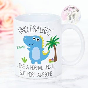 May include: White ceramic mug featuring a blue dinosaur illustration and the text "Unclesaurus Like a normal uncle, but more awesome".