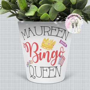 Könnte beinhalten: Weißer Keramik-Pflanztopf mit dem Text "Maureen Bingo Queen" in schwarzer und roter Schrift. Eine goldene Krone und Bingo-bezogene Bilder sind ebenfalls enthalten.
