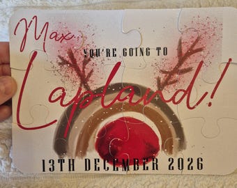Può includere: Un puzzle rettangolare con un design stampato raffigurante un arcobaleno, corna di renna e un cerchio rosso. Il testo recita Max, YOU'RE GOING TO Lapland!, e 13TH DECEMBER 2026. I pezzi del puzzle sono assemblati per mostrare l'immagine.