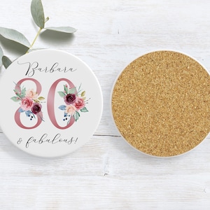Pu&ograve; includere: Sottobicchiere in ceramica bianca con un design floreale rosa e il testo "Barbara 80 & favolosa!"