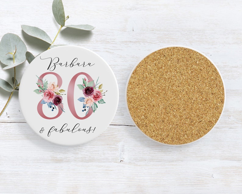 Pu&ograve; includere: Sottobicchiere in ceramica bianca con un design floreale rosa e il testo "Barbara 80 & favolosa!"