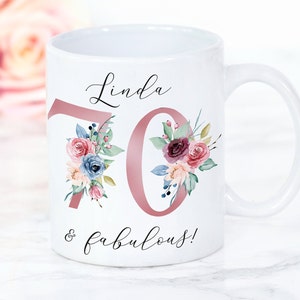 Puede incluir: Taza de cer&aacute;mica blanca con un dise&ntilde;o floral rosa y el texto "Linda 70 & fabulosa!"