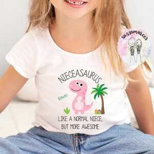 May include: White t-shirt with a pink dinosaur graphic and the text "Niec easaurus, like a normal niece, but more awesome".