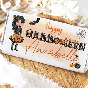 May include: A Halloween-themed chocolate bar wrapper featuring a cartoon girl with a pumpkin bucket. The words "happy HALLOWEEN Annabelle" are written in orange and black. A bat, spiderwebs, and pumpkins decorate the wrapper.