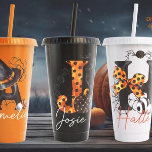 Könnte beinhalten: Drei wiederverwendbare Halloween-Becher mit Strohhalmen. Die Becher sind orange, schwarz und weiß mit verschiedenen Designs. Der orange Becher hat einen Hexenhut und den Buchstaben "A" mit dem Namen "Amelie" darunter. Der schwarze Becher hat einen gepunkteten Buchstaben "J" mit dem Namen "Josie" darunter. Der weiße Becher hat eine Spinne und eine Schleife mit dem Buchstaben "H" und dem Namen "Halle" darunter.