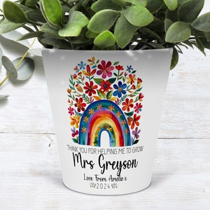 Peut inclure: Pot en céramique blanche avec un motif arc-en-ciel et fleurs. Le texte indique "Merci de m'avoir aidé à grandir Mme Greyson Avec amour d'Amélie x 2024".