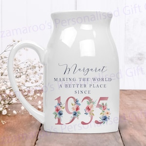 May include: White ceramic mug with a handle, featuring a floral design and the text "Margaret Making the World a Better Place Since 1935".
