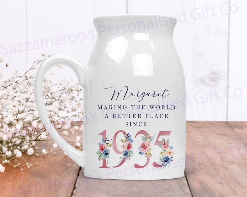 May include: White ceramic mug with a handle, featuring a floral design and the text "Margaret Making the World a Better Place Since 1935".