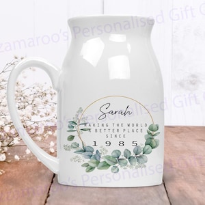 May include: White ceramic mug with a gold circle around the text "Sarah Making the World a Better Place Since 1985". The mug has a green and white floral design.