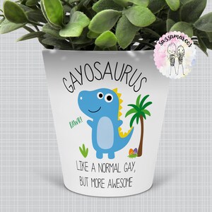 May include: White ceramic planter with a blue dinosaur illustration and the text "Gayosaurus, Like a normal gay, but more awesome".