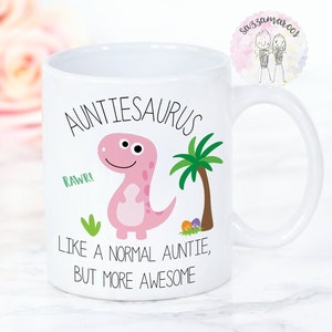 May include: White ceramic mug with a pink dinosaur illustration and the text "Auntiesaurus". The mug also features the phrases "Rawr!" and "Like a normal auntie, but more awesome."
