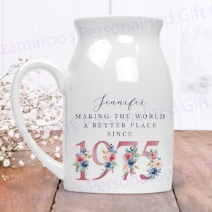 May include: White ceramic mug with a blue and pink floral design. The mug has a handle and says "Jennifer Making the World a Better Place Since 1975".