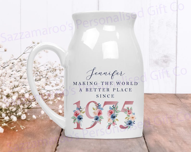 May include: White ceramic mug with a blue and pink floral design. The mug has a handle and says "Jennifer Making the World a Better Place Since 1975".