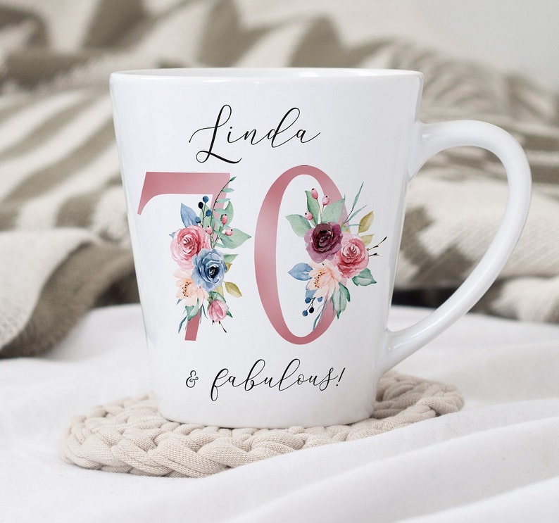 May include: White ceramic mug with a pink floral design and the text "Linda 70 & fabulous!"