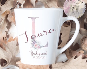 May include: White ceramic mug with a pink and purple floral design and the letter L. The mug says "Laura Bridesmaid 25.07.2020".