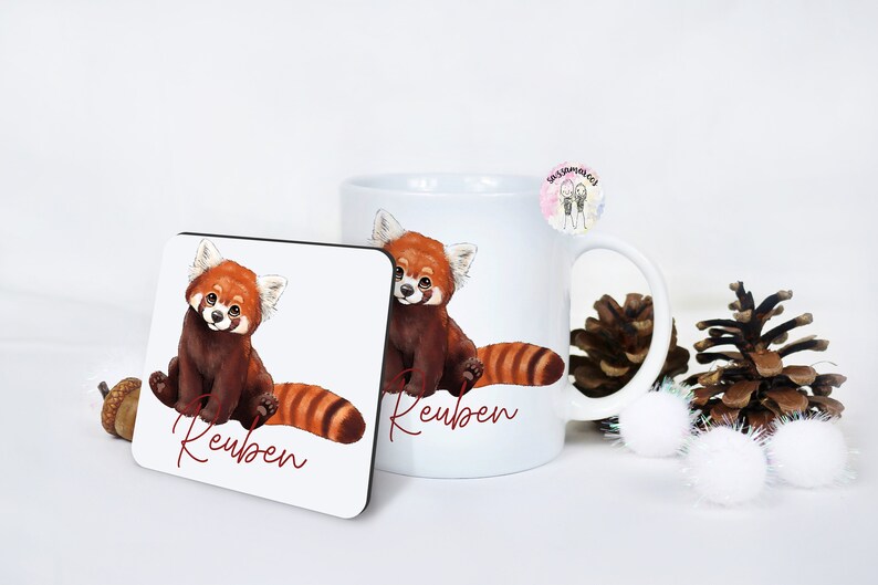 Puede incluir: Taza de cer&aacute;mica blanca con una ilustraci&oacute;n de panda rojo y el nombre "Reuben" impreso en ella. Tambi&eacute;n se muestra un posavasos a juego con el mismo dise&ntilde;o.