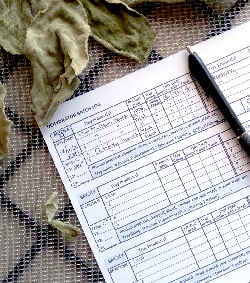 Op de afbeelding: Een close-up van een wit vel papier met een handgeschreven dehydrator batch log. De log bevat kolommen voor datum, tijd, temperatuur, product op de lade, productvoorbereiding, ladebekleding en droogtijd. De log is ingevuld met verschillende kruiden en bladeren, waaronder bladeren van  verbascum,  comfrey  en rozemarijn.