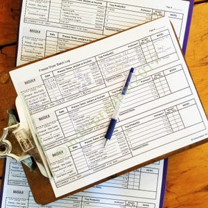 Pu&ograve; includere: Un modulo di registrazione dei lotti di liofilizzazione con una penna blu in cima. Il modulo ha colonne per il numero di lotto, la data, i tempi di processo, i prodotti del vassoio, pre congelati, peso e note. Il modulo viene utilizzato per tenere traccia del processo di liofilizzazione di vari alimenti.
