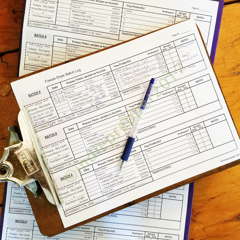 Pu&ograve; includere: Un modulo di registrazione dei lotti di liofilizzazione con una penna blu in cima. Il modulo ha colonne per il numero di lotto, la data, i tempi di processo, i prodotti del vassoio, pre congelati, peso e note. Il modulo viene utilizzato per tenere traccia del processo di liofilizzazione di vari alimenti.