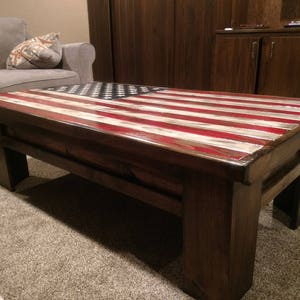May include: A wooden coffee table with a red, white, and blue American flag design on the top. The table has a dark brown stain and a glossy finish.