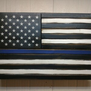 May include: A wooden American flag with a blue line, representing support for law enforcement. The flag is made of individual wood planks, painted black and white, with a blue stripe across the bottom.