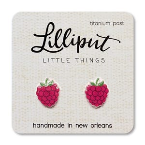 May include: A pair of raspberry-shaped stud earrings with titanium posts, presented on a textured card. The card features the text "Lilliput LITTLE THINGS" and "handmade in new orleans". The earrings are bright pink with green leaves.