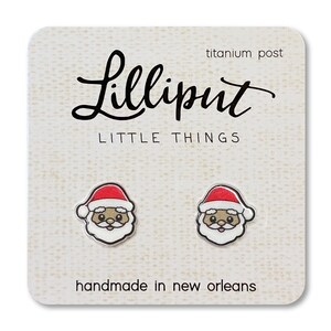 May include: A pair of small, white, Santa Claus earrings with red hats and black eyes. The earrings are on a white card with the text "Lilliput Little Things" and "handmade in new orleans".