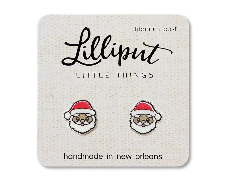 May include: A pair of small, white, Santa Claus earrings with red hats and black eyes. The earrings are on a white card with the text "Lilliput Little Things" and "handmade in new orleans".