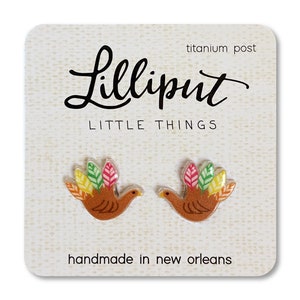 May include: A pair of turkey-shaped earrings with colorful feathers. The earrings are made of resin and have titanium posts. The card reads "Lilliput Little Things" and "handmade in New Orleans".