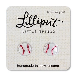 May include: A pair of white baseball earrings with red stitching. The earrings are on a card that says "Lilliput Little Things" and "handmade in New Orleans".