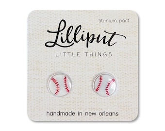May include: A pair of white baseball earrings with red stitching. The earrings are on a card that says "Lilliput Little Things" and "handmade in New Orleans".