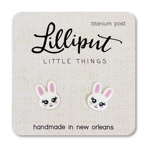 May include: White bunny rabbit stud earrings with pink ears and black eyes. The earrings are on a white card with the text "Lilliput Little Things" and "titanium post" and "handmade in new orleans".