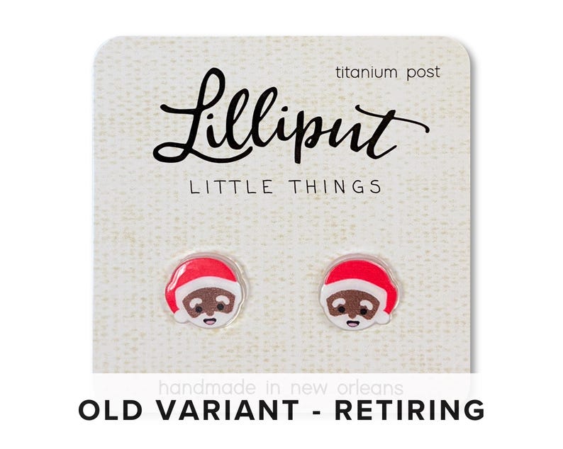 May include: A pair of earrings featuring a cartoon Santa Claus with a red hat and brown face. The earrings are made of polymer clay and have titanium posts. The card reads "Lilliput Little Things" and "Old Variant - Retiring".