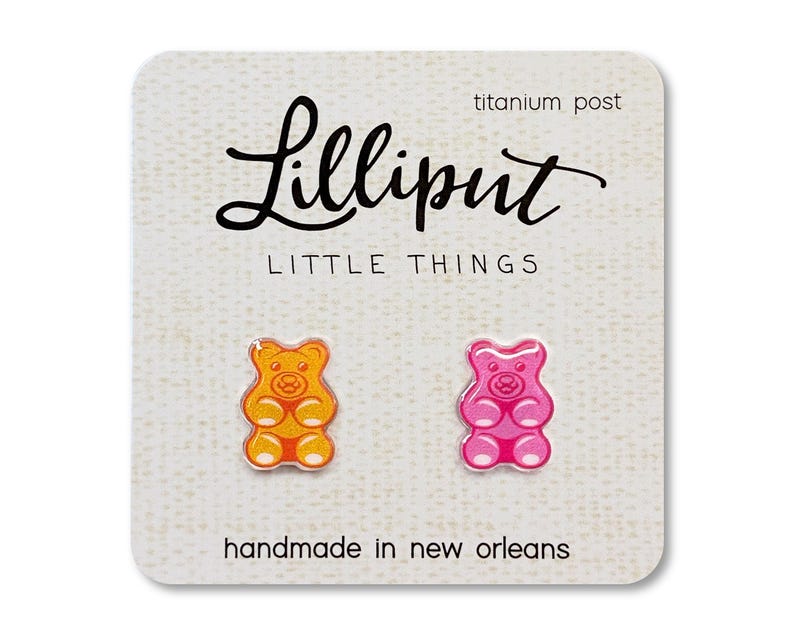 Op de afbeelding: Gummy bear oorknopjes in oranje en roze, gepresenteerd op een getextureerde kaart. De kaart leest "Lilliput Little Things" en "handmade in new orleans". De oorbellen hebben titanium pinnen.